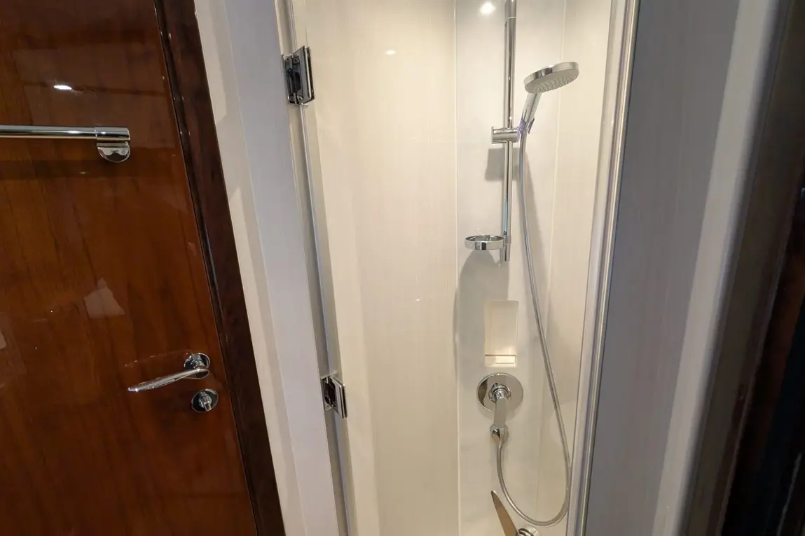 Shower cubicle featuring chrome fixtures, a handheld showerhead, and a glass door against white tiled walls.