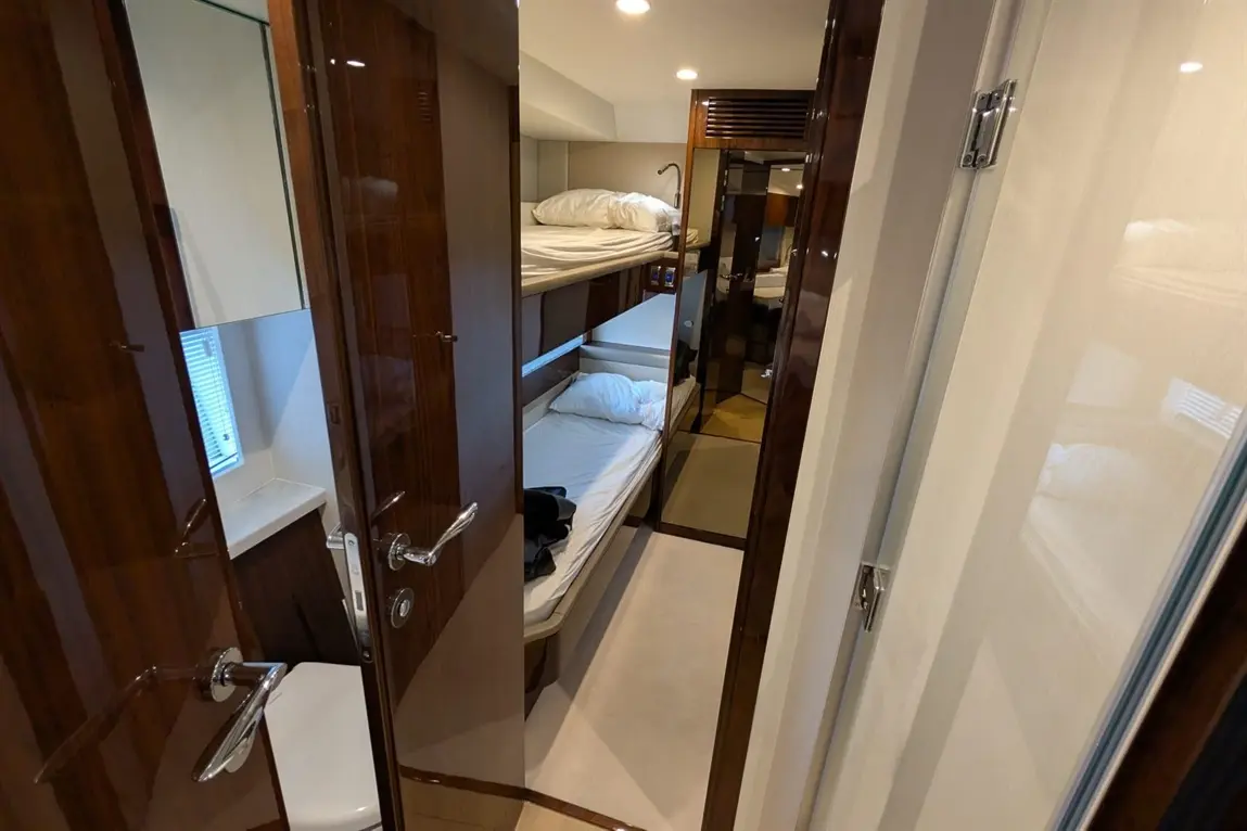 Interior view of a modern yacht cabin with bunk beds and a bathroom door, featuring wooden finishes and soft lighting.
