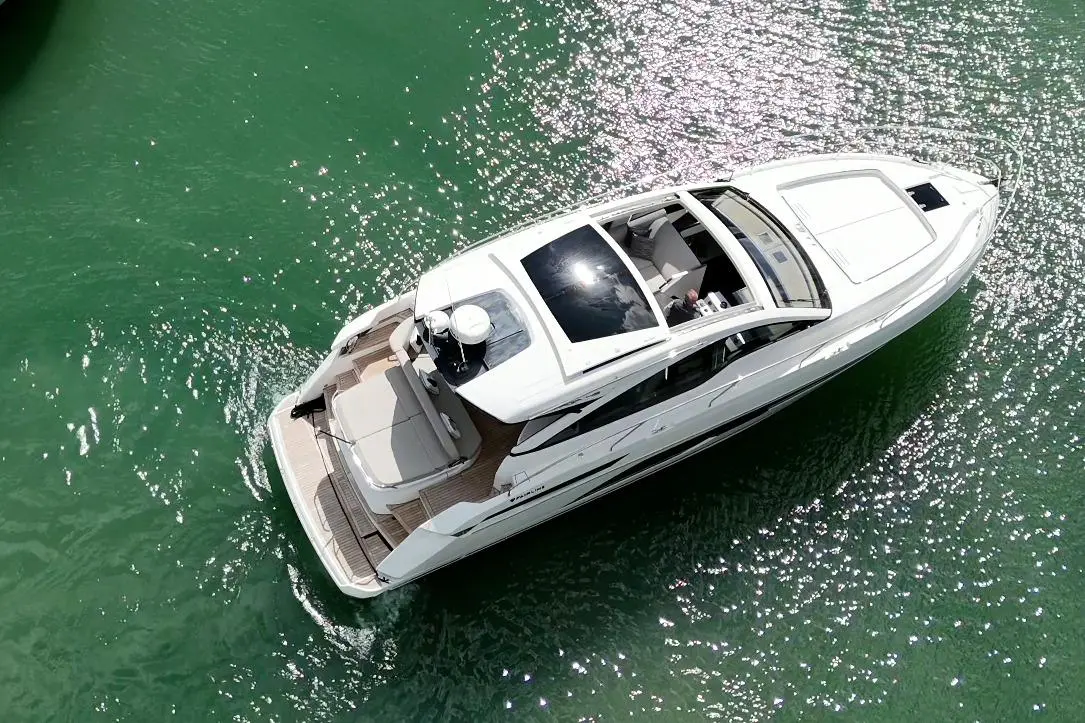 A sleek white motor yacht glides over sparkling green water, showcasing a spacious sun deck and modern interior.