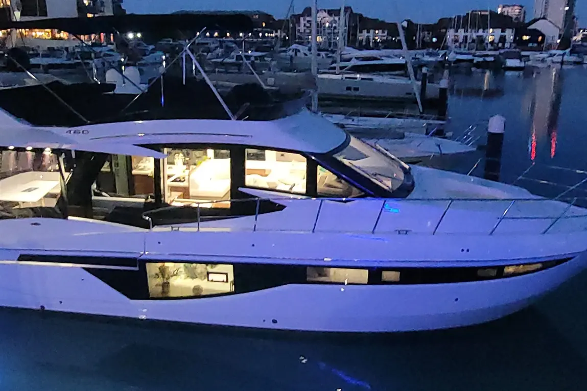 Luxury yacht moored at a marina during twilight, showcasing interior lights and nearby boats in the background.