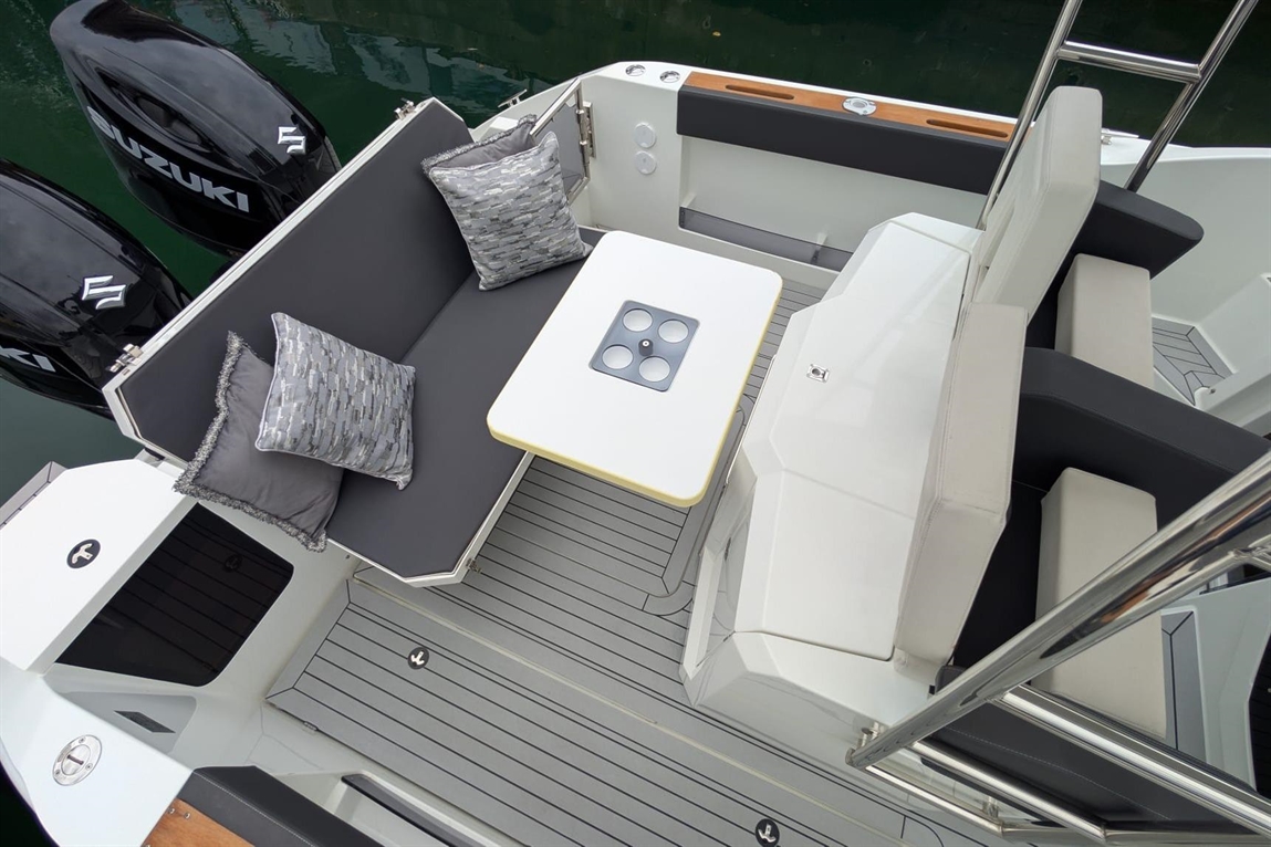 Stylish boat seating area with gray cushions, a white table, and black Suzuki motors in the background, set on a sleek deck.