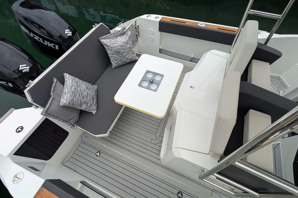 Stylish boat seating area with gray cushions, a white table, and black Suzuki motors in the background, set on a sleek deck.