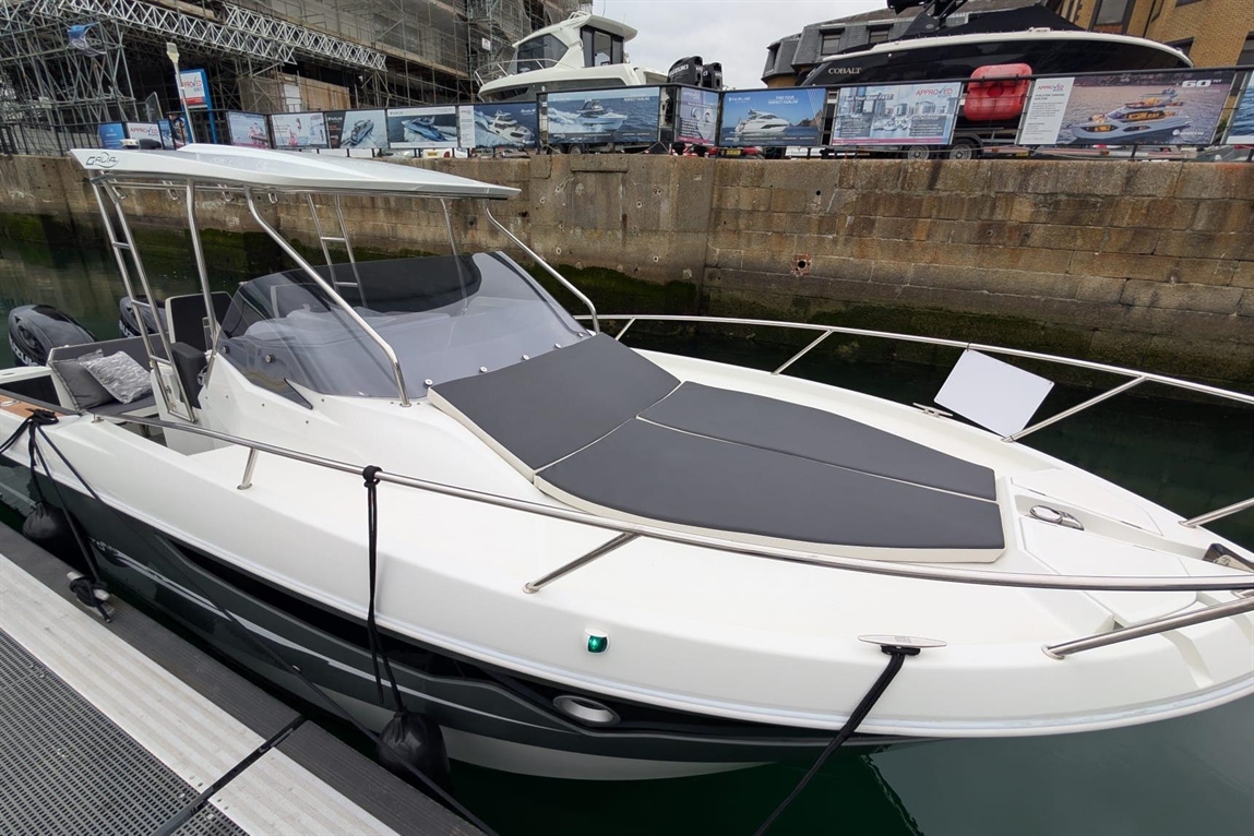 A sleek white boat with gray cushions docked at a marina, featuring a semi-open design and surrounding boats in the background.