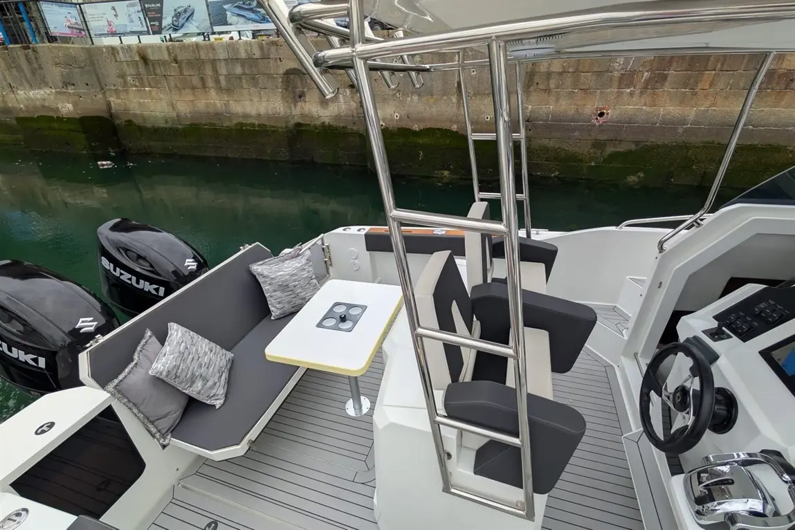 Modern boat interior featuring grey seating, a table, and Suzuki outboard engines beside a calm waterway.