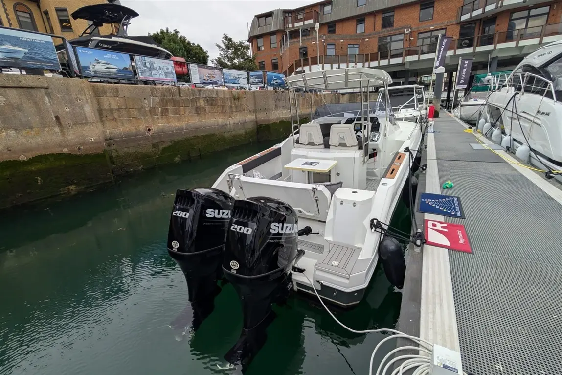 A sleek motorboat with two Suzuki 200 outboard engines docked at a marina beside promotional banners and a walkway.