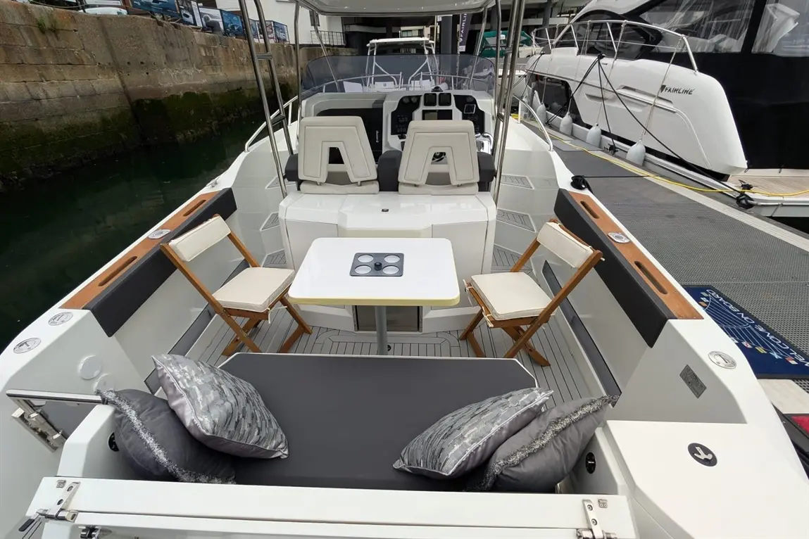 Modern boat interior featuring a dining table, two chairs, a cushioned bench, and decorative pillows by the dock.