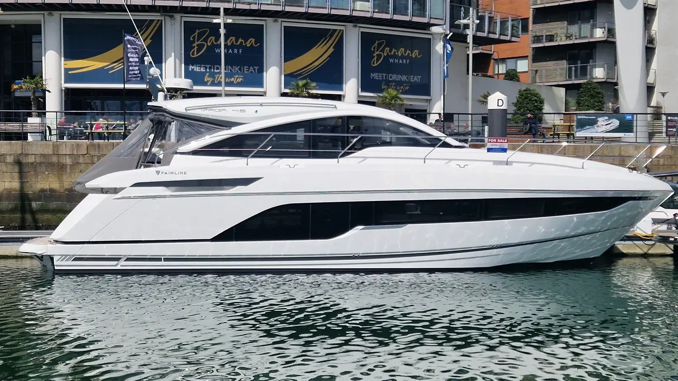 A sleek white Fairline yacht docked at Banana Wharf, with diners visible in the background and a 