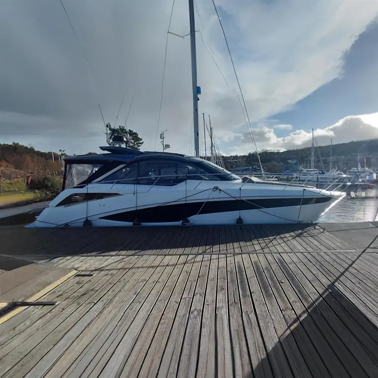 A sleek white and black motorboat docked on wooden planks, with a marina and cloudy sky in the background.
