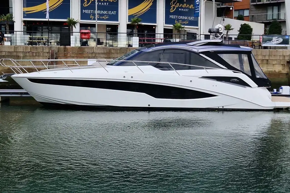 A sleek white motorboat docked beside Banana Wharf, reflecting on calm water with modern architecture in the background.