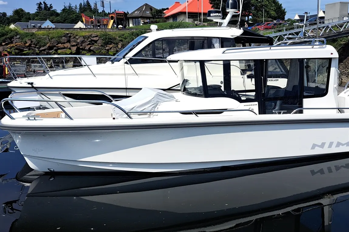 A white motorboat named "Nimbus" docked beside a larger white yacht in a marina under a clear blue sky.