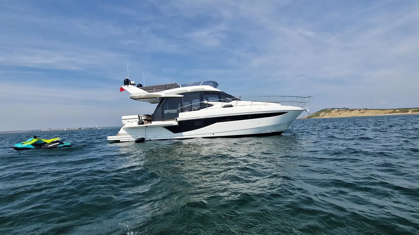A sleek white motorboat floats on water, with a bright blue and green jet ski nearby under a clear blue sky.
