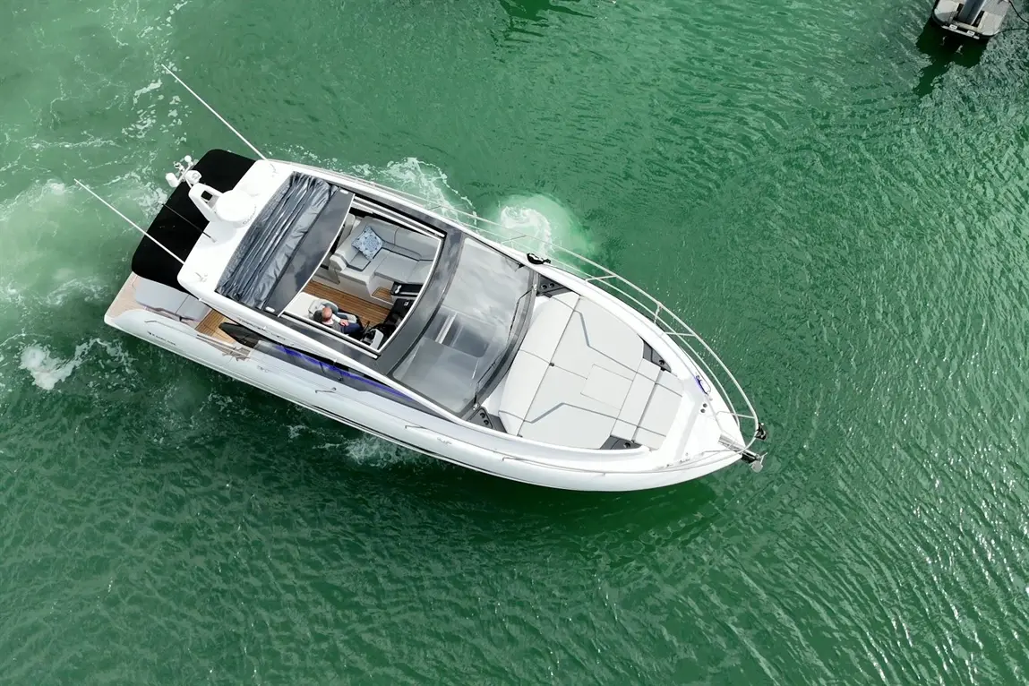 Aerial view of a white motorboat gliding through green water, with a person seated in the cockpit, enjoying a leisure trip.