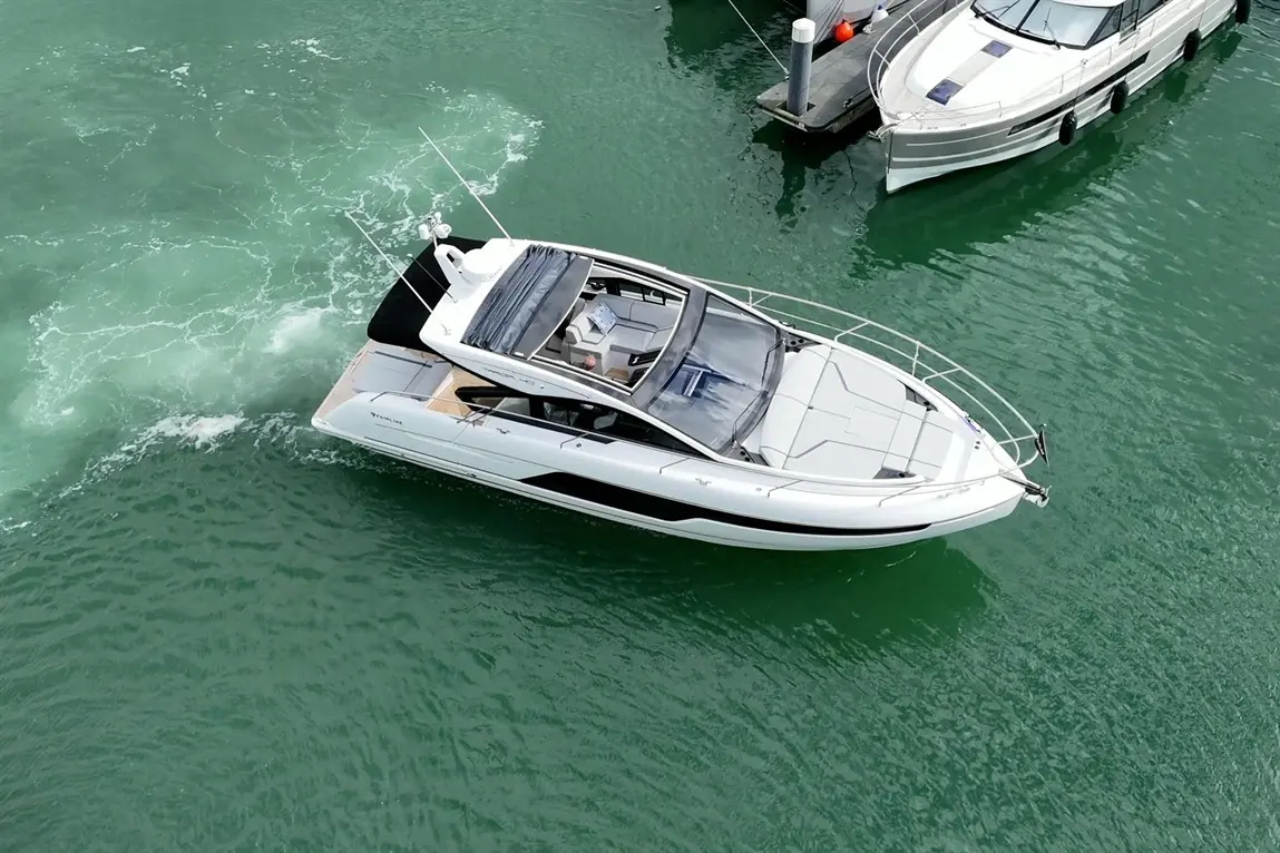 Motorboat navigating through turquoise water, with visible wake and nearby parked boats in a marina setting.