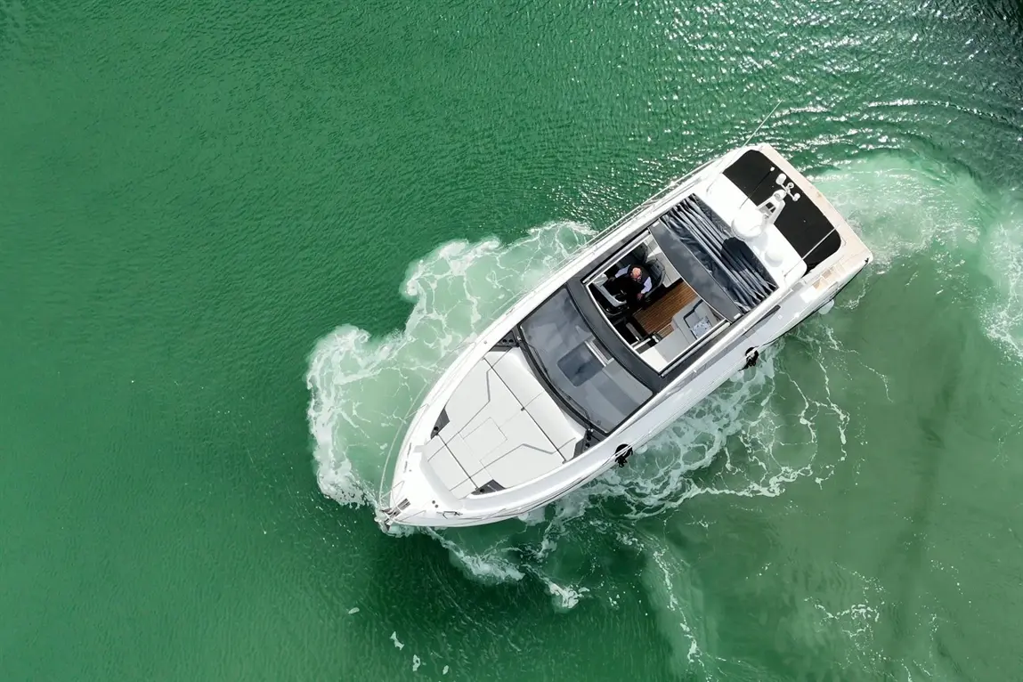 Aerial view of a luxury motorboat navigating through clear green water, with a man seated at the helm.