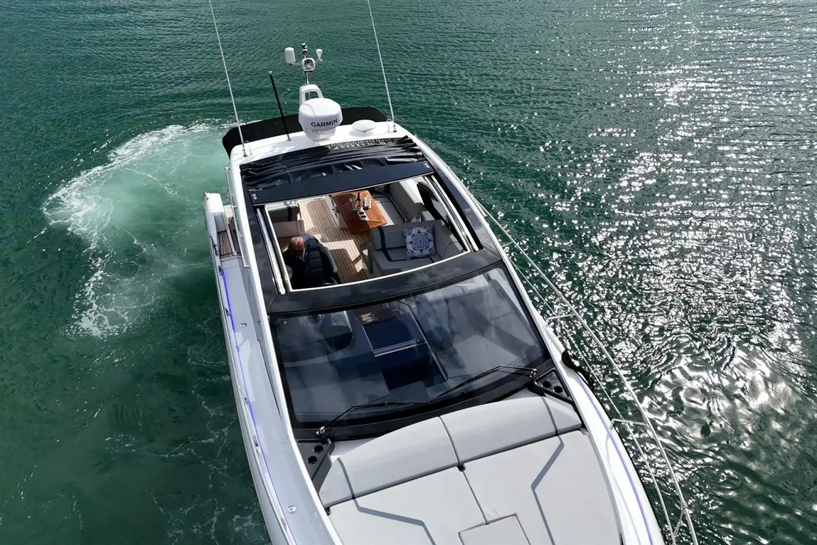 A luxury yacht navigating turquoise waters with a person seated indoors, featuring a Garmin navigation system on top.