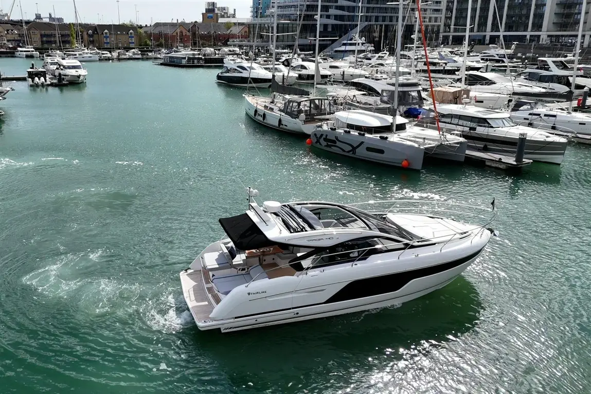A sleek motorboat navigates a marina bustling with various yachts and boats against a clear turquoise water backdrop.