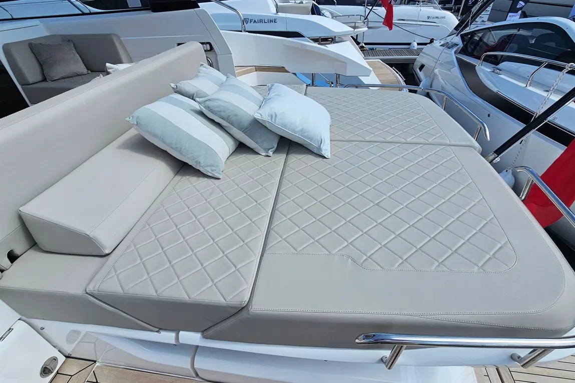 Luxury boat lounge area with plush cushions on a padded deck, surrounded by sleek yachts in the marina.