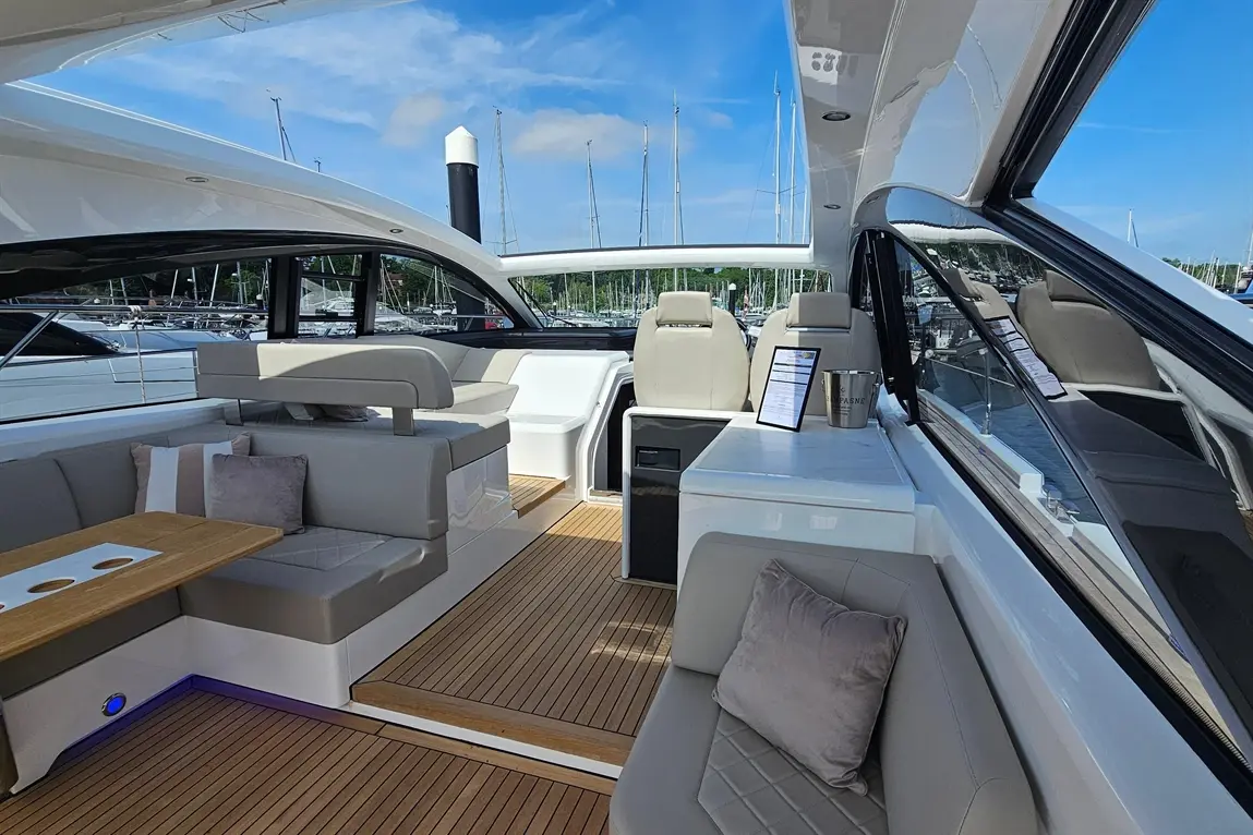Stylish yacht interior with plush seating, a wooden table, and a menu; views of a marina and blue sky in the background.