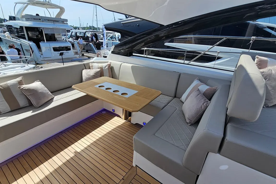 Luxury yacht seating area with plush cushions and a wooden table, overlooking a marina filled with boats.