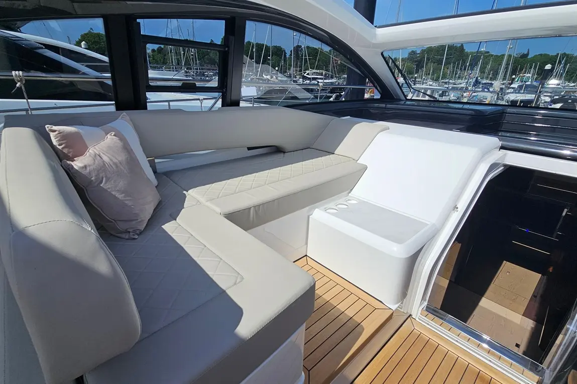 Luxurious boat interior featuring cushioned seating, a white cooler, and scenic views of a marina with masts in the background.