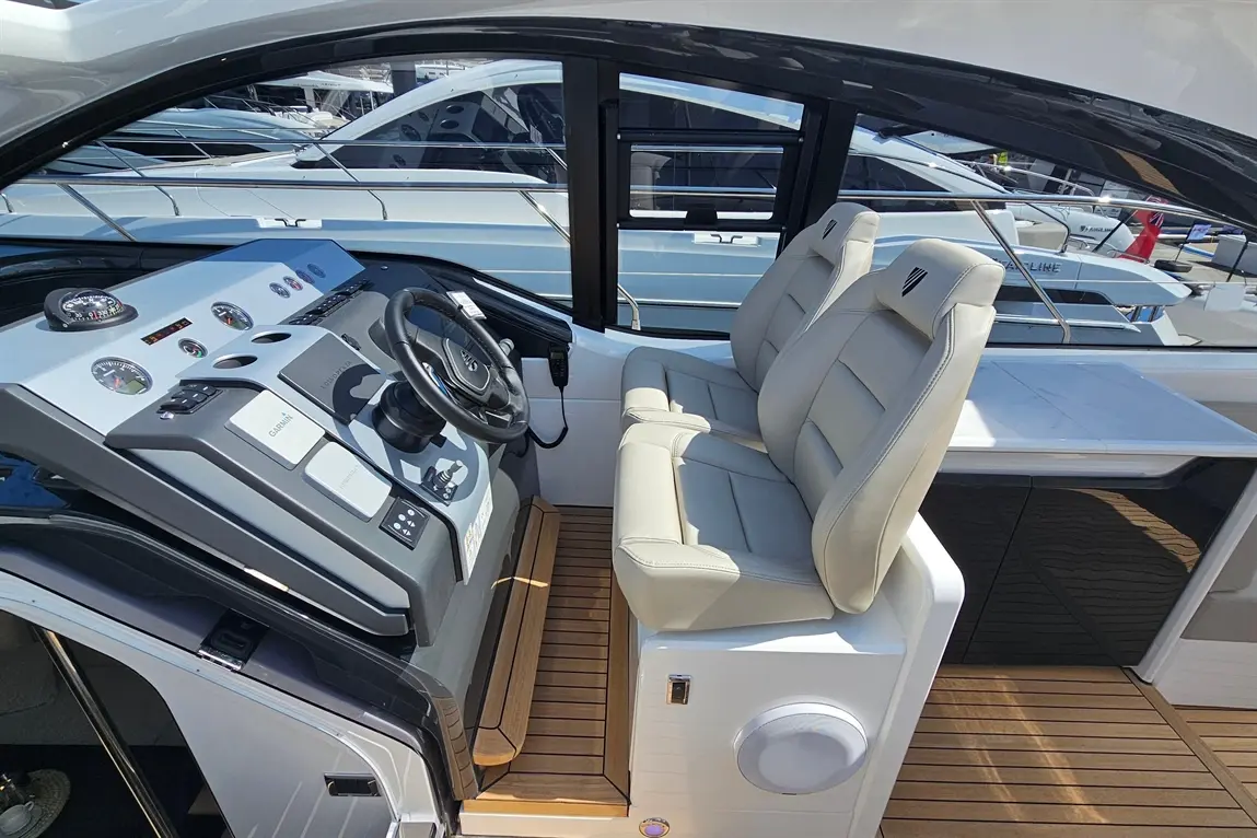 Modern yacht cockpit featuring two plush seats, a steering wheel, and navigation controls, overlooking other boats.