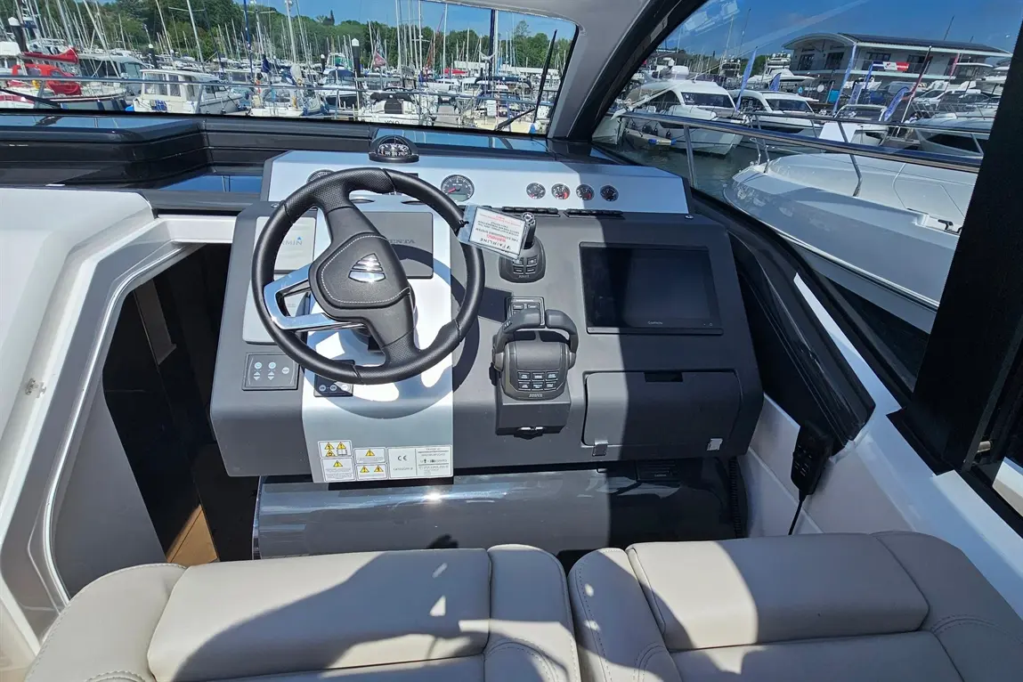 View of a modern boat's dashboard featuring a steering wheel, control panel, and navigation screen at a marina.