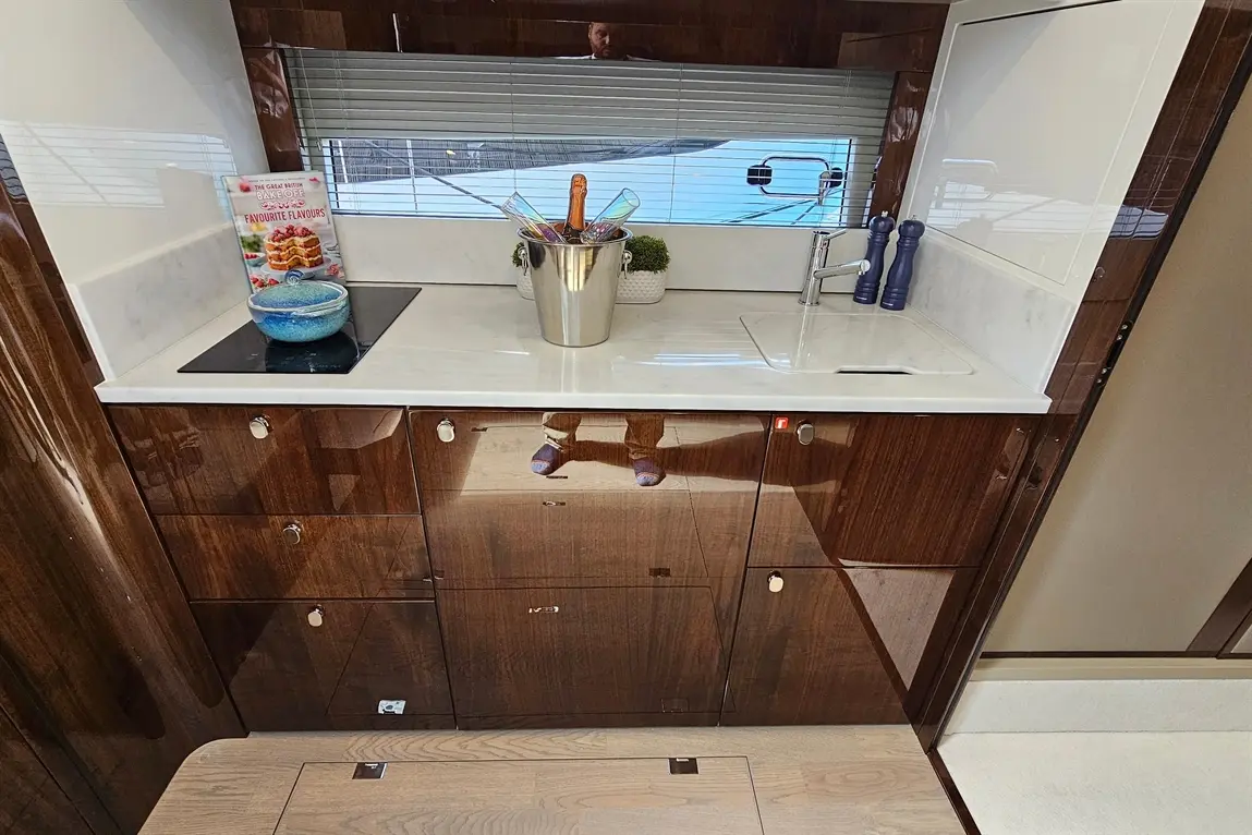 Modern kitchen with polished wood finish, utensils, wine in a bucket, and a recipe book on a marble countertop.