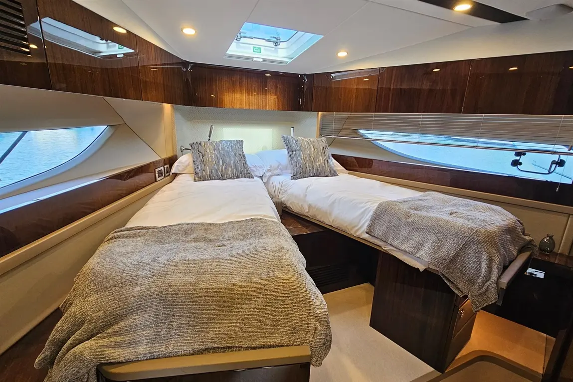 Luxurious twin beds with plush pillows and throw blankets in a yacht cabin, featuring wood finishes and a view of the water.