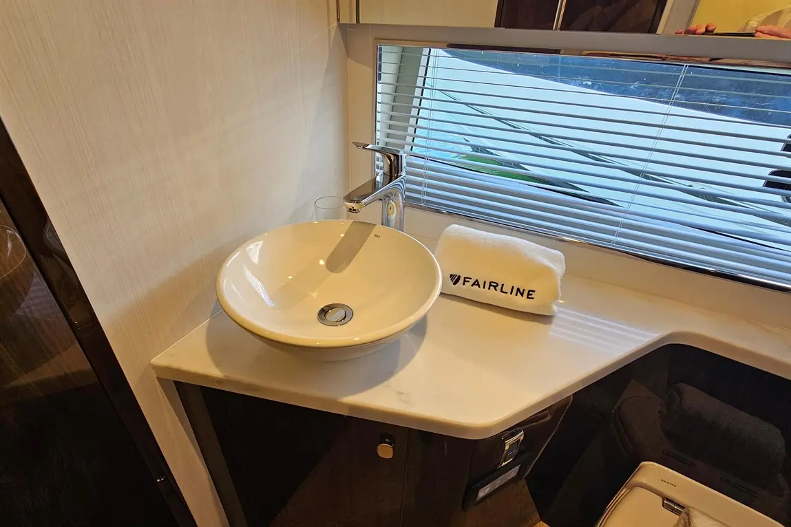 Modern bathroom sink with a round bowl, sleek tap, and a towel marked 'FAIRLINE' beside a window with blinds.