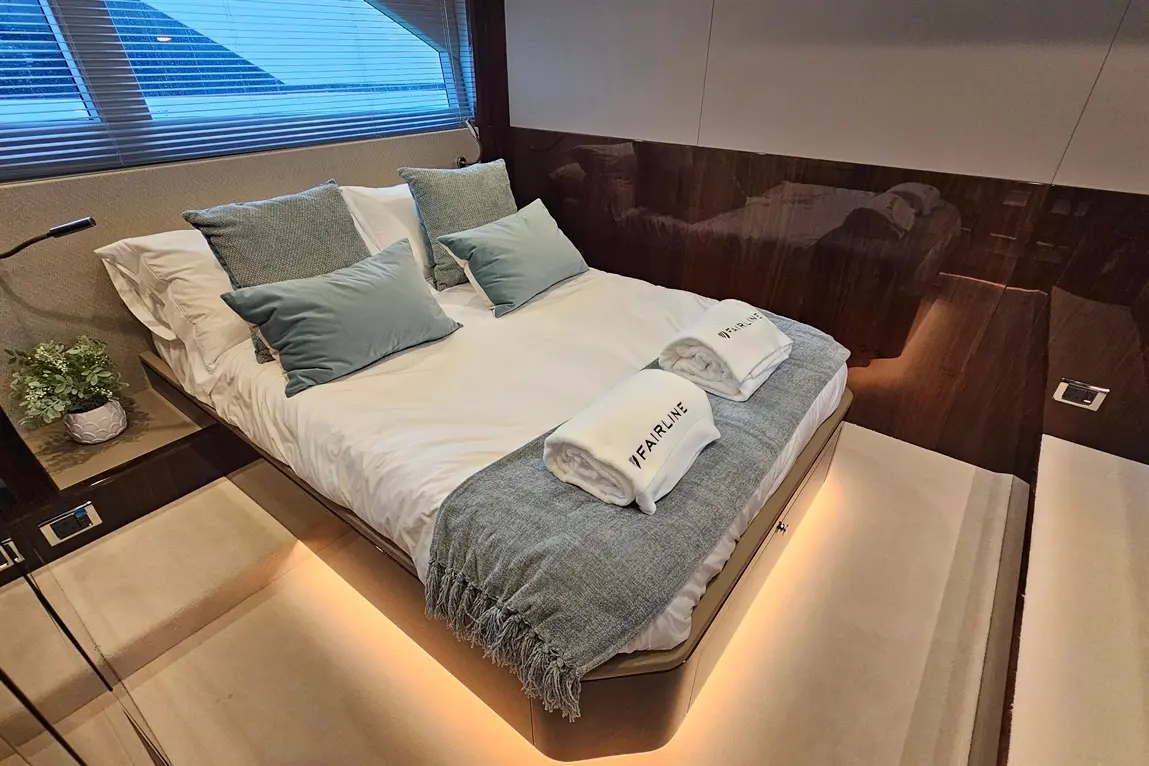Elegant bedroom with a double bed, plush pillows, and towels labelled 'FAIRLINE', enhanced by warm ambient lighting.