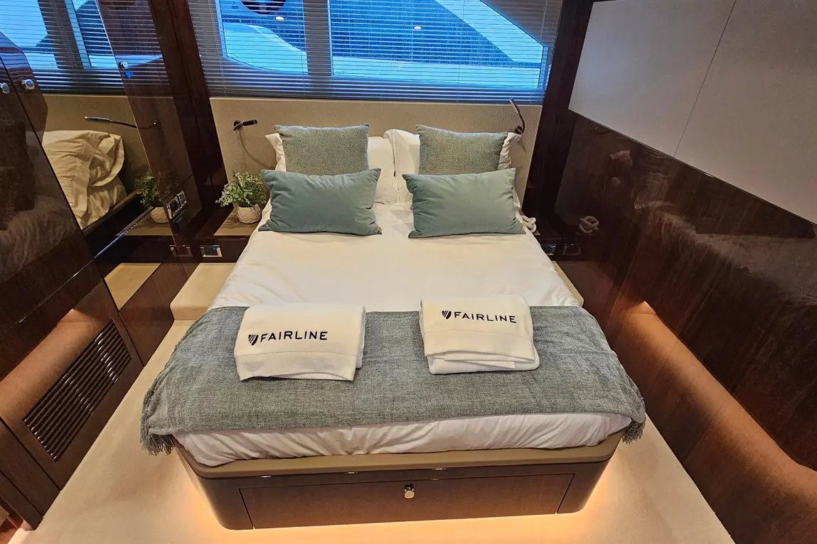 Elegant boat cabin featuring a double bed with Fairline branded towels, plush pillows, and a view from a large window.