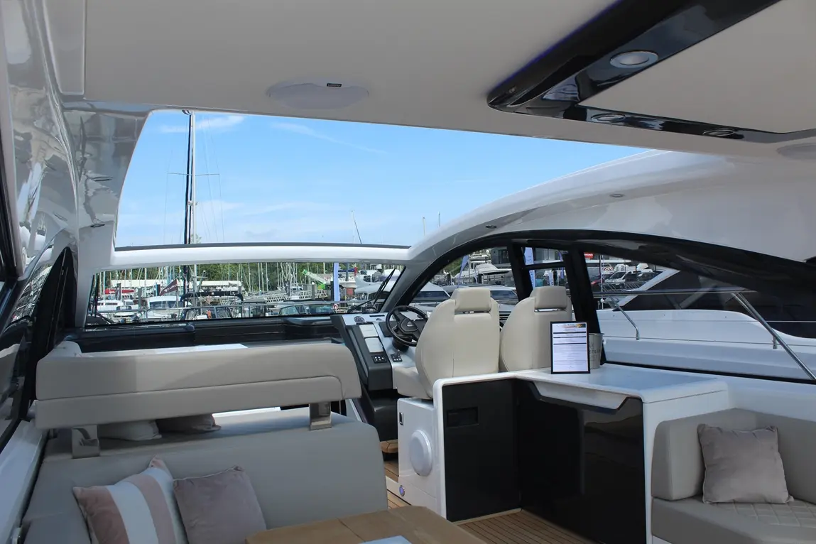 Luxury yacht interior with modern seating, navigation controls, and views of the marina under a clear blue sky.