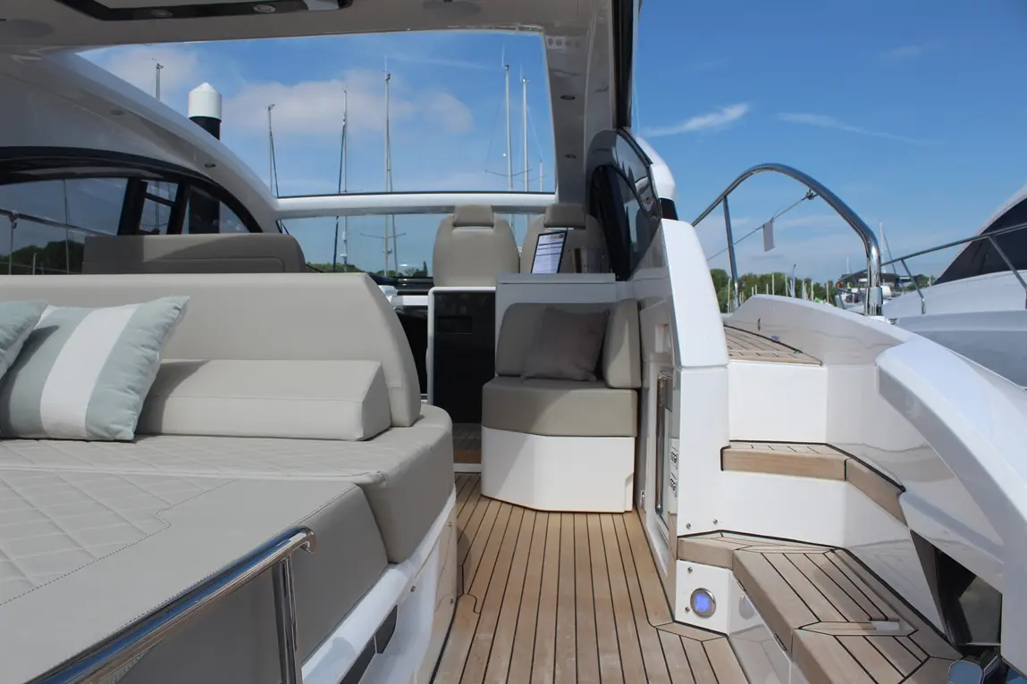 Luxury yacht interior featuring plush seating, wooden deck, and a view of moored boats under a clear blue sky.