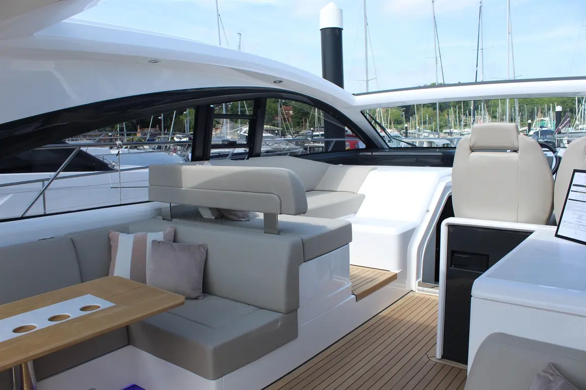 Luxury yacht interior featuring plush seating, a wooden table, and a view of boats at a marina.