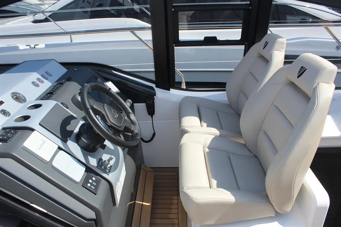 Boat cockpit featuring a steering wheel, control panel, and two comfortable white seats with a wood floor.