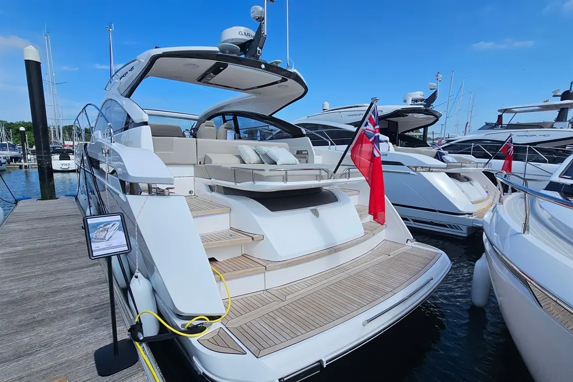 Luxury yacht docked at marina, featuring wooden steps, plush seating, and British flag; surrounded by other boats.