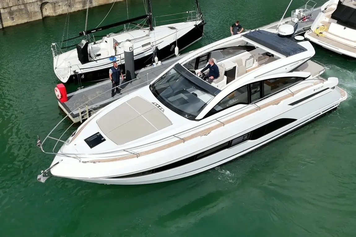 Luxury motorboat docked in green waters, with two men on the dock and one steering, showcasing elegant design and features.