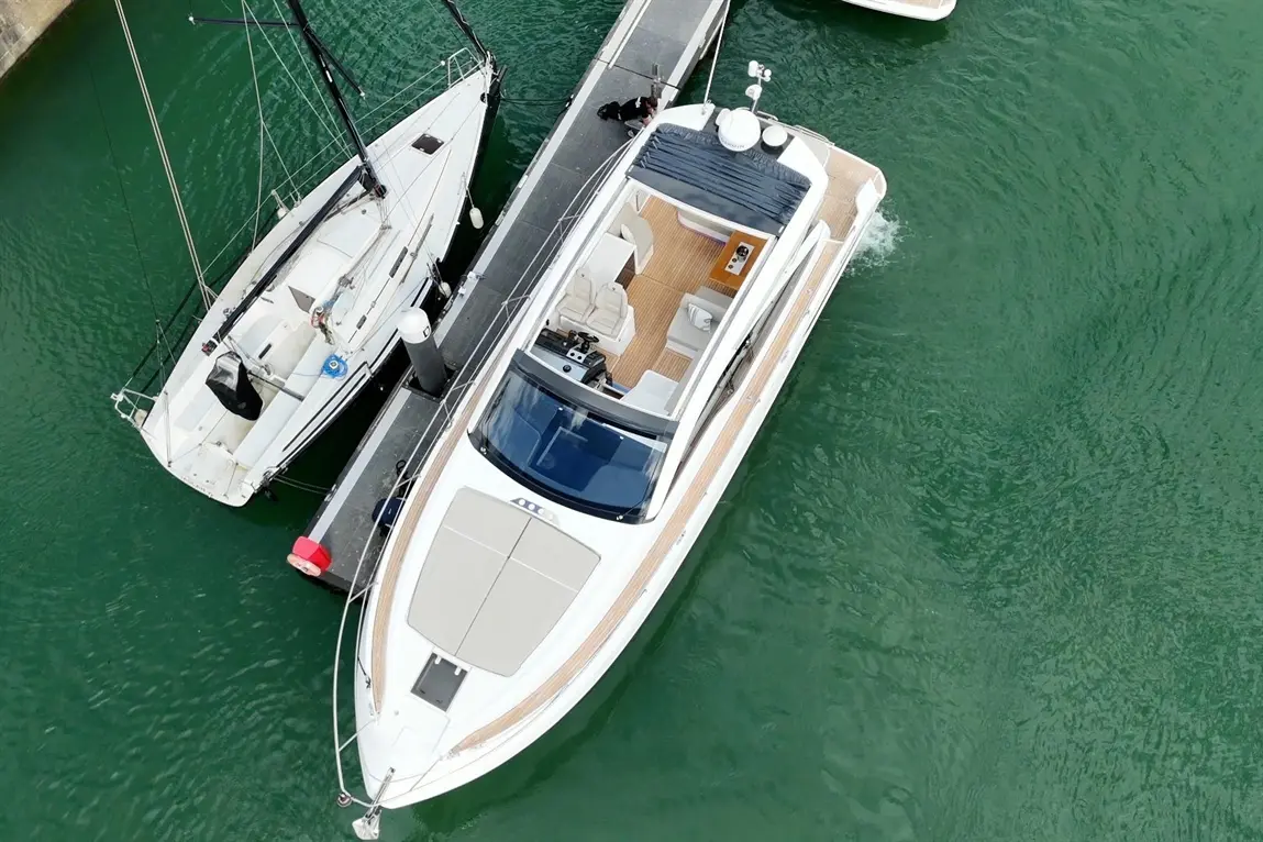 Aerial view of a sleek motorboat at a dock, alongside a white sailboat in turquoise water, showcasing luxury marine design.