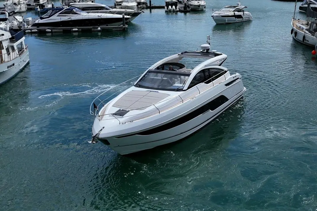Luxury motorboat cruising in a marina surrounded by smaller yachts on clear blue water.