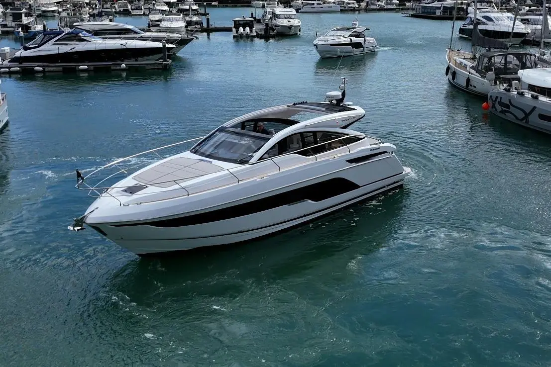 A sleek white motor yacht navigates a marina, surrounded by various boats and clear blue waters.