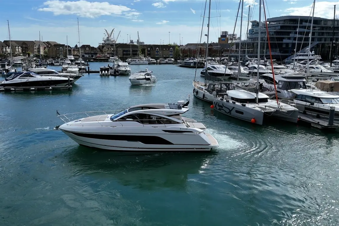 A white motorboat navigates through a marina filled with various yachts and boats under a sunny sky.