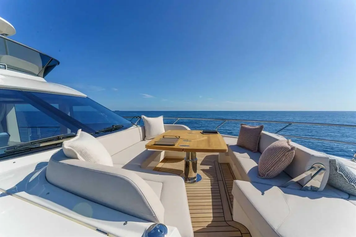 Luxe yacht deck with plush seating and wooden table overlooking serene ocean under clear blue sky.