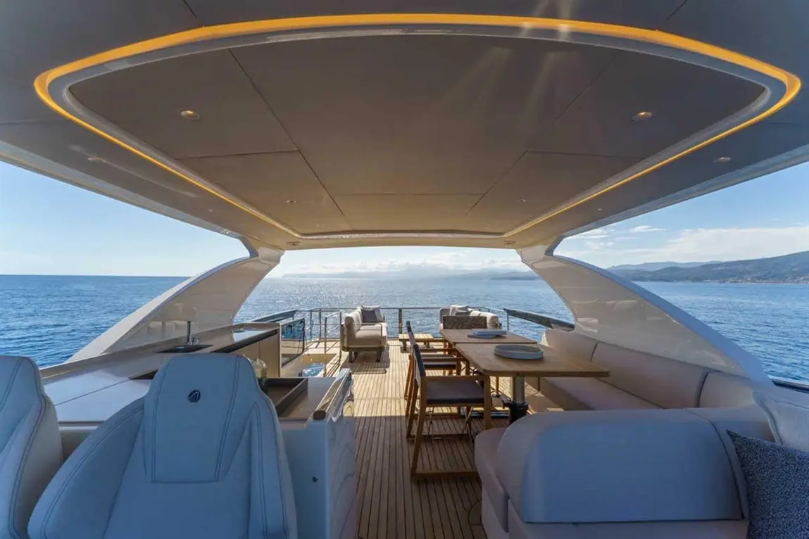 Luxurious yacht interior with seating, dining area, and panoramic sea views under a bright sky.