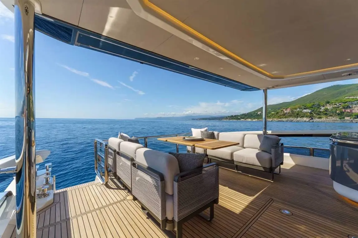 Luxurious yacht deck with modern seating, wooden table, and stunning ocean views under a clear blue sky.