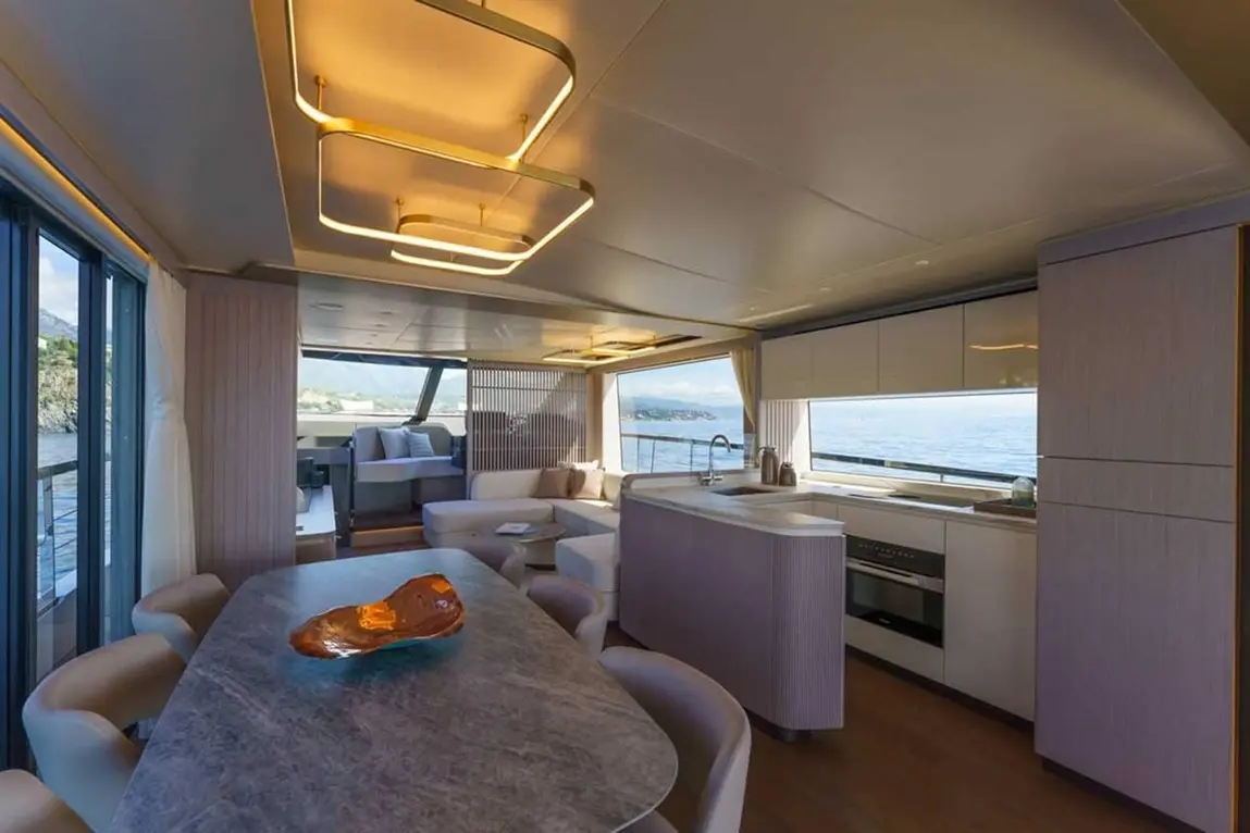 Modern yacht interior showcasing a stylish lounge area, dining table, and kitchen with large windows and sea views.