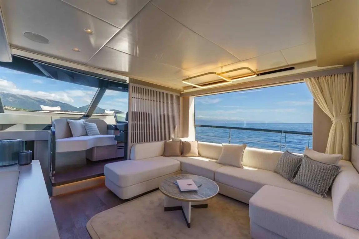 Modern yacht interior featuring a spacious lounge with a white sofa, glass windows, and a scenic ocean view.