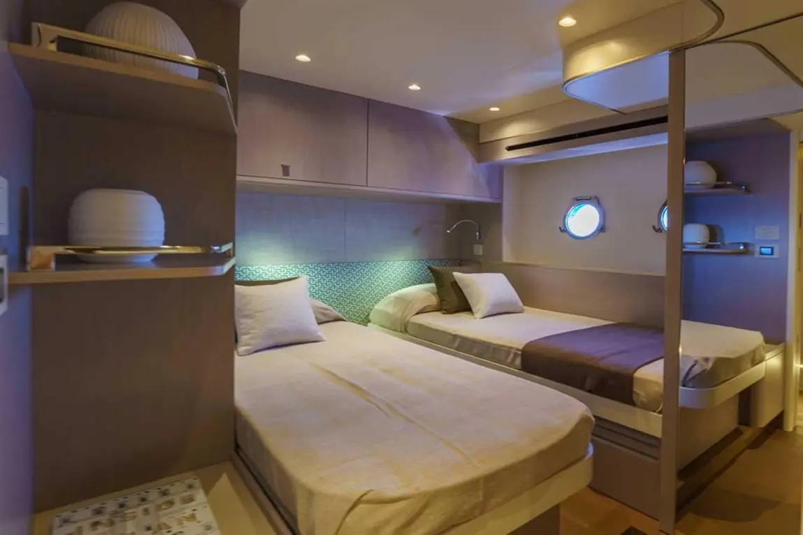 Modern twin bedroom with wooden accents, ambient lighting, and round porthole windows, featuring two beds and decorative pillows.