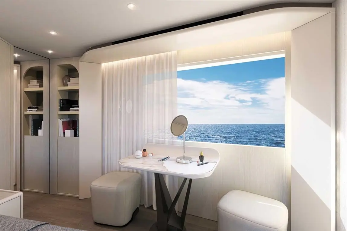 Modern cabin with a table, mirror, and ocean view. Shelves hold books, and curtains frame the scenic window.