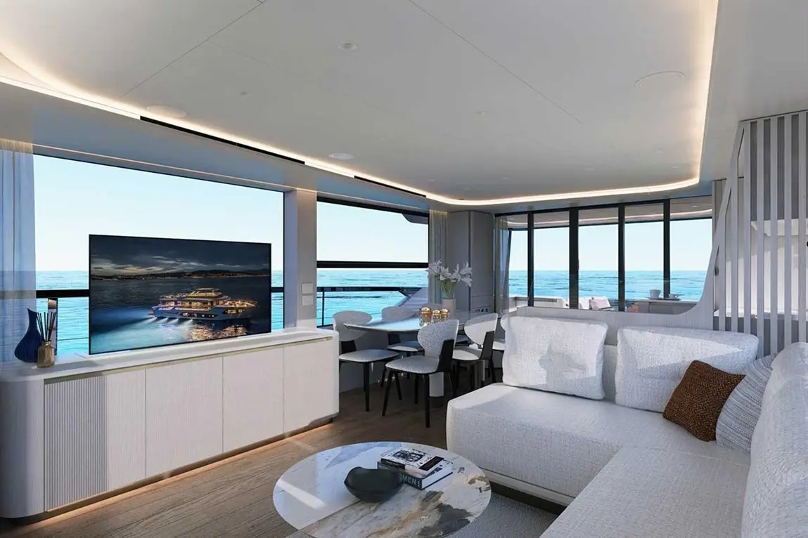 Luxurious yacht interior with a modern sofa, dining area, and panoramic windows overlooking the ocean and a TV showing a yacht.