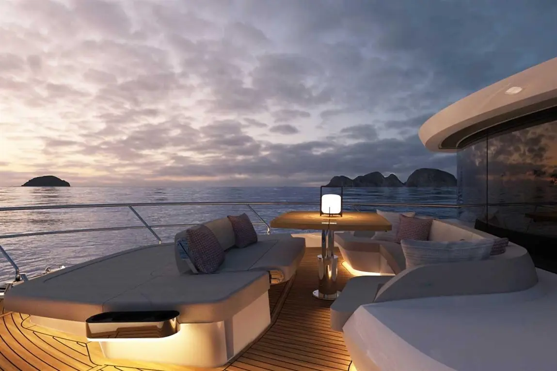 Luxury yacht deck at sunset, featuring a table with a lamp, modern seating, and distant islands on a calm sea.